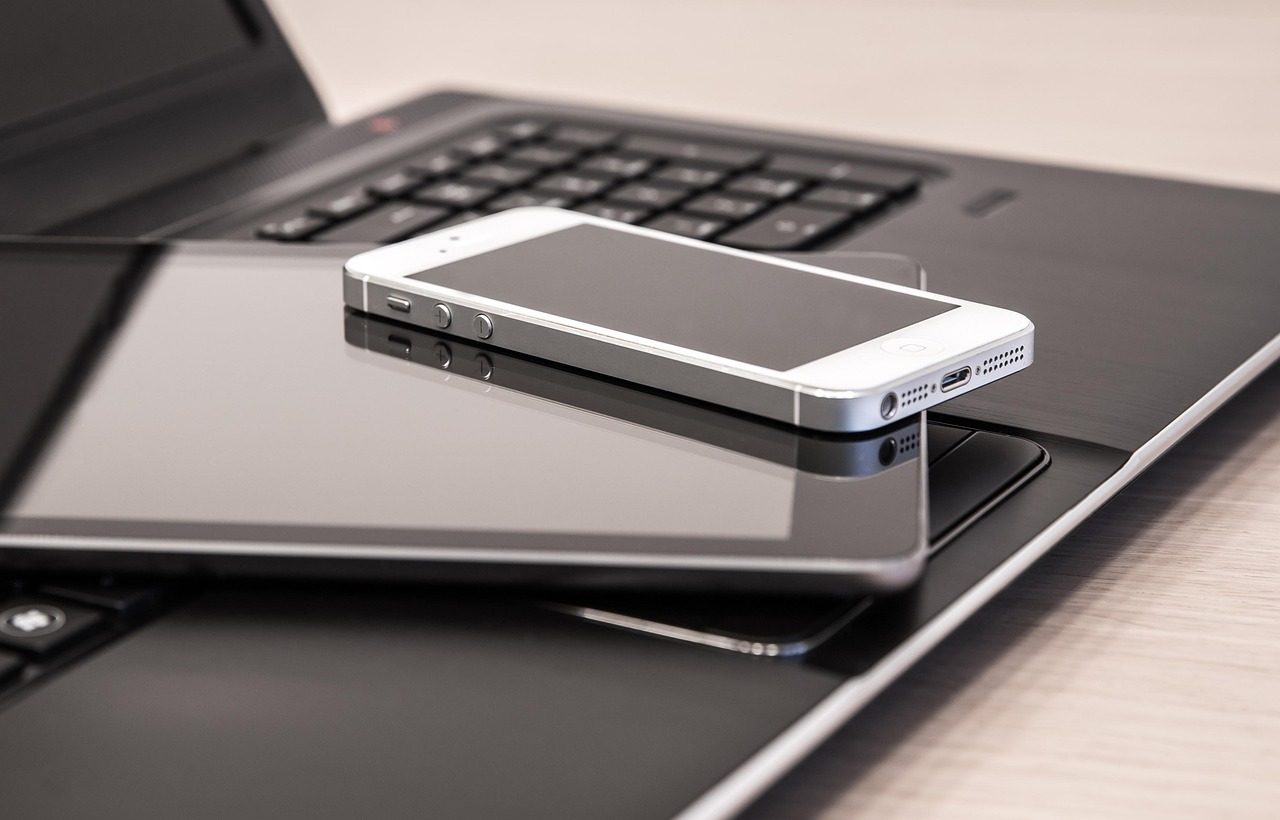 Büro-Werkzeuge. Ein Laptop, ein Tablet und ein Smart-Phone liegen aufeinander gestapelt auf dem Tisch.